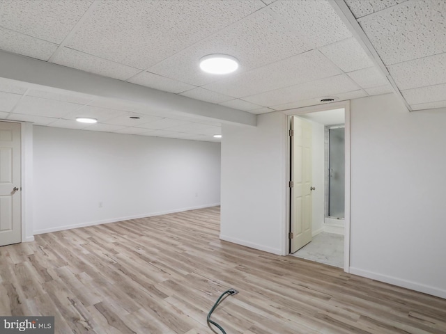 finished basement with a drop ceiling, light wood-type flooring, and baseboards