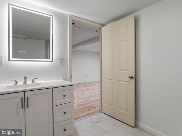 bathroom with baseboards, a paneled ceiling, marble finish floor, and vanity