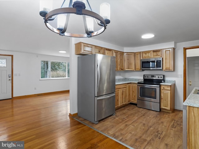 kitchen with wood finished floors, appliances with stainless steel finishes, an inviting chandelier, baseboards, and hanging light fixtures