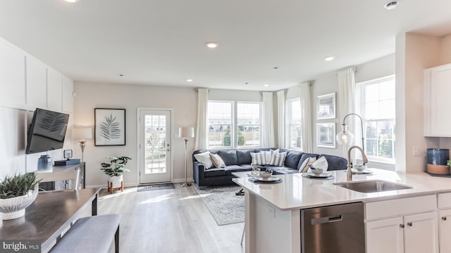 kitchen with open floor plan, stainless steel dishwasher, light wood-style floors, white cabinetry, and a sink