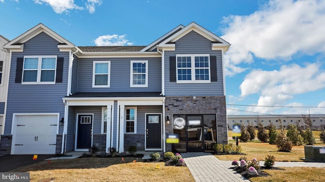 townhome / multi-family property featuring a front yard, a garage, and stone siding