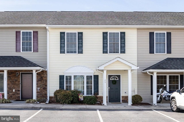 multi unit property with stone siding, roof with shingles, and uncovered parking