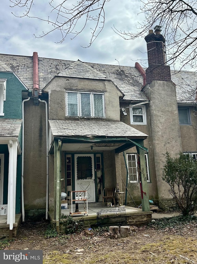 view of front of home featuring a high end roof, stucco siding, a porch, and a chimney