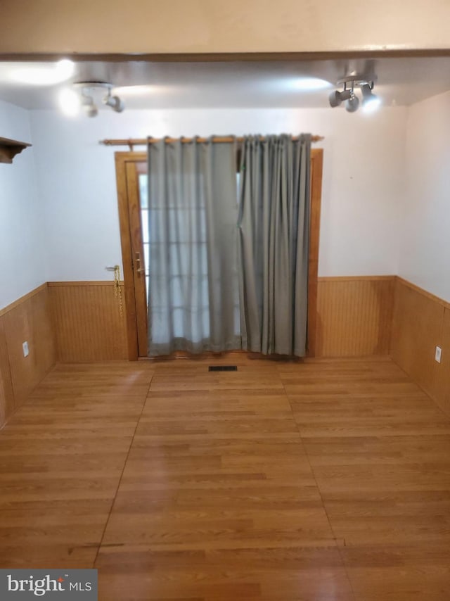 empty room with a wainscoted wall, visible vents, and wood finished floors