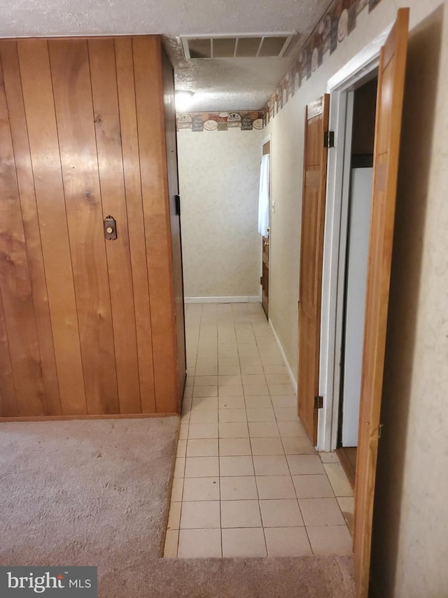 hallway with visible vents, light carpet, wood walls, and light tile patterned flooring