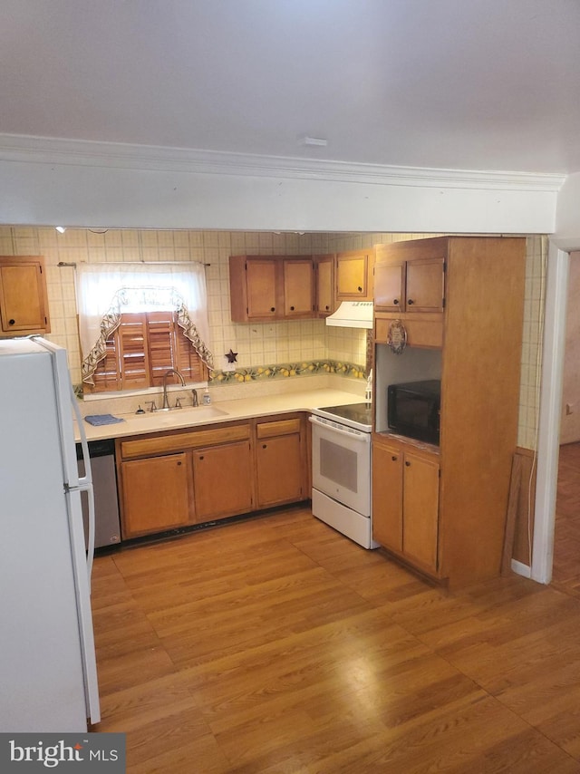 kitchen with a sink, backsplash, white appliances, light wood-style floors, and exhaust hood