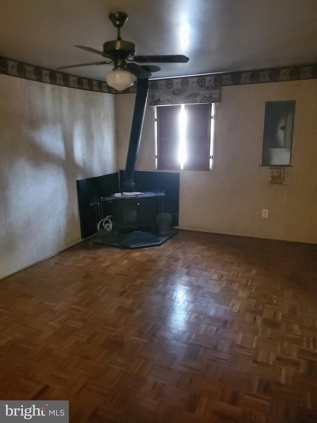 unfurnished living room with electric panel, a ceiling fan, and a wood stove