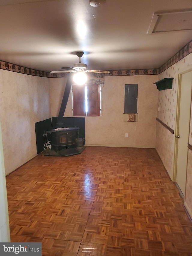 interior space with electric panel, a wood stove, and a ceiling fan