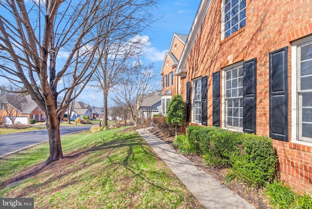 view of side of home with a residential view, brick siding, and a lawn