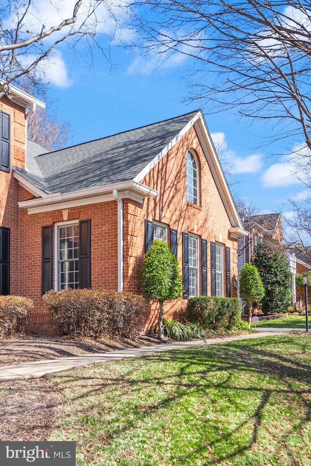 view of property exterior featuring brick siding, a lawn, and a shingled roof