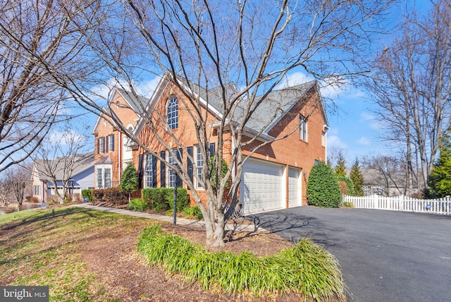 traditional home with aphalt driveway, brick siding, an attached garage, and fence