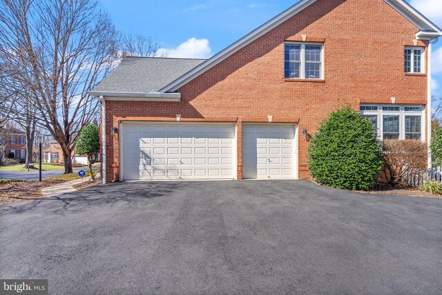 view of side of property featuring aphalt driveway, a garage, brick siding, and roof with shingles