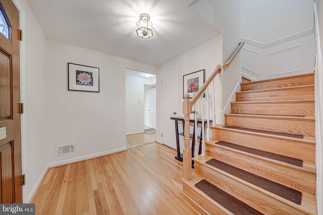 foyer entrance with wood finished floors, visible vents, baseboards, stairs, and a decorative wall