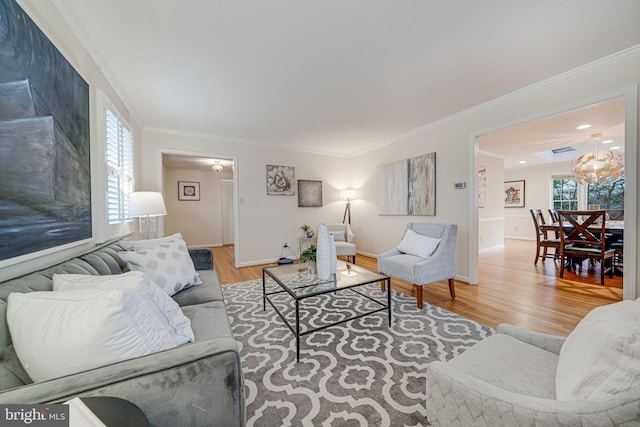 living area featuring a notable chandelier, wood finished floors, baseboards, and ornamental molding