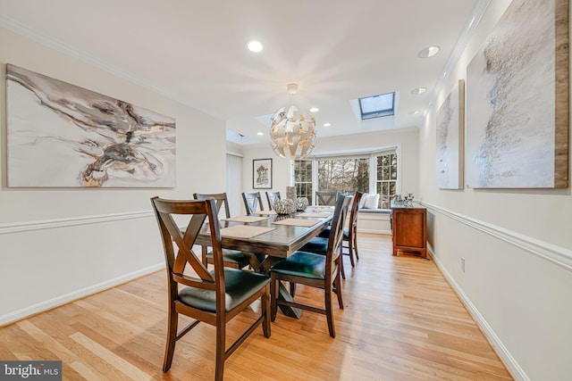 dining space featuring crown molding, baseboards, light wood-type flooring, a skylight, and an inviting chandelier