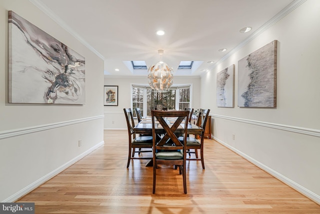 dining area with a skylight, light wood-style floors, an inviting chandelier, and ornamental molding