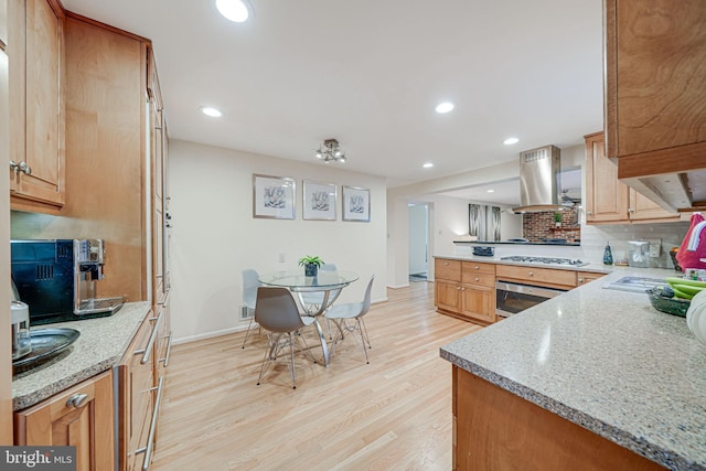 kitchen featuring island exhaust hood, a sink, wall oven, a peninsula, and light wood finished floors