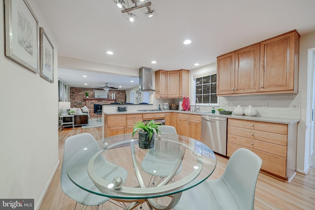 kitchen with a peninsula, stainless steel dishwasher, wall chimney exhaust hood, light wood-type flooring, and backsplash