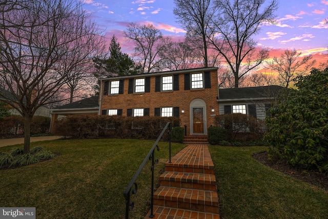 colonial-style house featuring a yard and brick siding