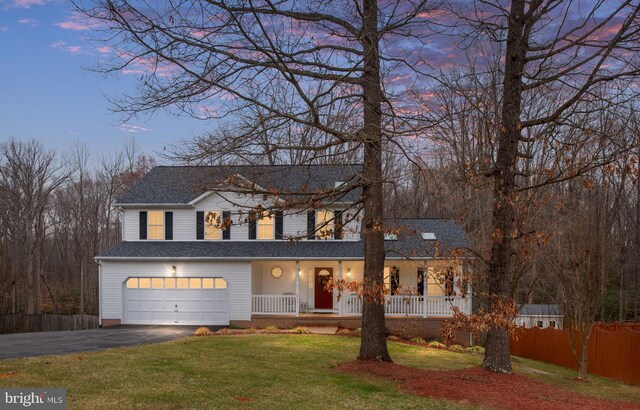 traditional-style home with fence, driveway, an attached garage, covered porch, and a front lawn