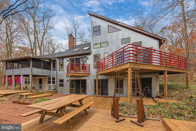 back of house with outdoor dining area, a deck, a chimney, and a sunroom