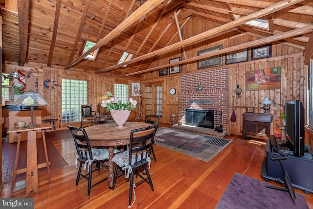 dining area featuring beamed ceiling, wood-type flooring, wood walls, wooden ceiling, and a brick fireplace