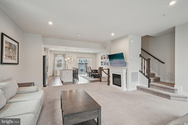 living room featuring stairway, visible vents, baseboards, recessed lighting, and light colored carpet