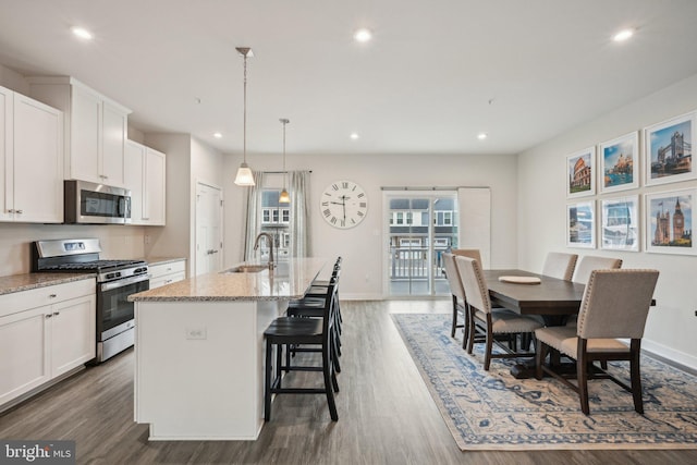 kitchen featuring dark wood-type flooring, an island with sink, a sink, stainless steel appliances, and white cabinets