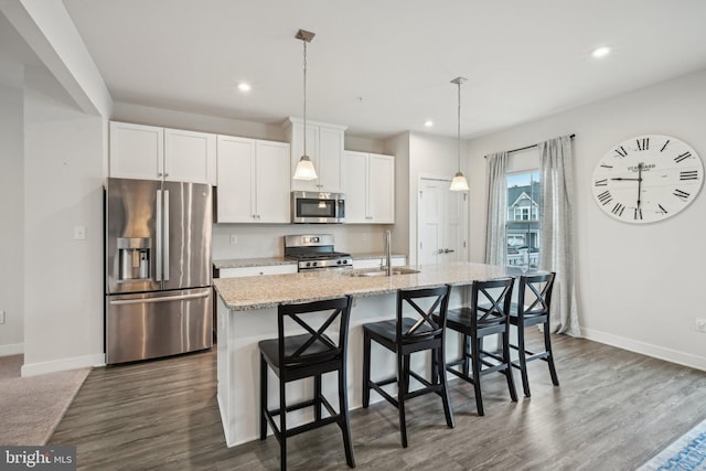 kitchen featuring baseboards, a kitchen island with sink, a sink, stainless steel appliances, and white cabinets