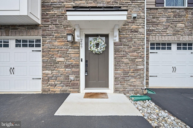 view of exterior entry featuring a garage, stone siding, and driveway