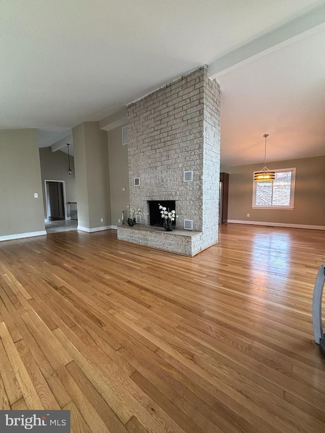 unfurnished living room with visible vents, lofted ceiling with beams, wood finished floors, a fireplace, and baseboards