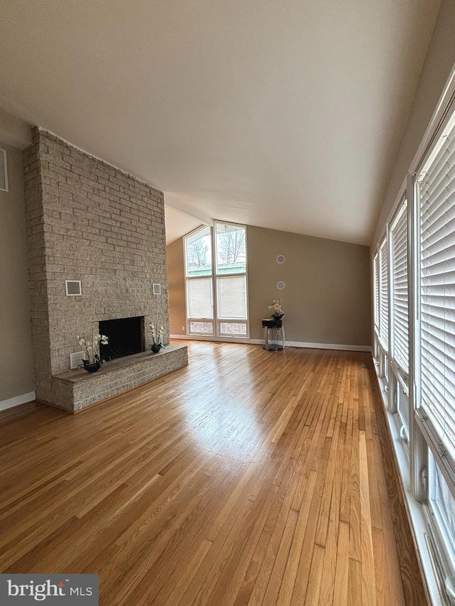 unfurnished living room featuring hardwood / wood-style floors, lofted ceiling, a fireplace, and baseboards