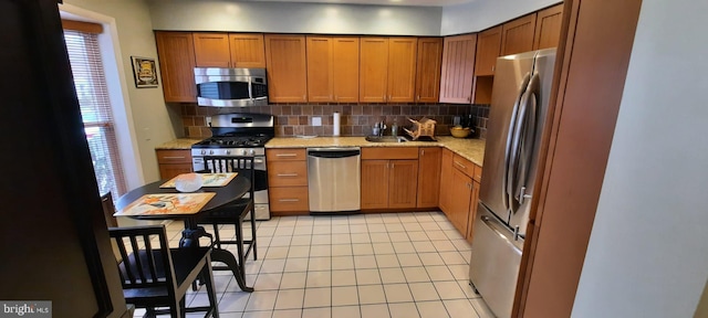 kitchen with tasteful backsplash, light tile patterned floors, light stone counters, brown cabinetry, and stainless steel appliances