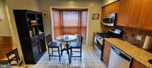 kitchen featuring light stone counters, brown cabinets, backsplash, and stainless steel appliances