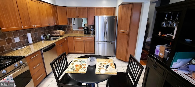 kitchen with light stone counters, backsplash, appliances with stainless steel finishes, brown cabinetry, and light tile patterned floors