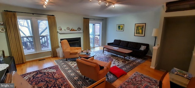 living room featuring track lighting, visible vents, baseboards, wood finished floors, and a glass covered fireplace