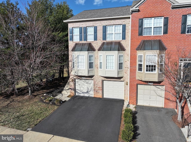 view of property featuring brick siding, an attached garage, a shingled roof, and driveway