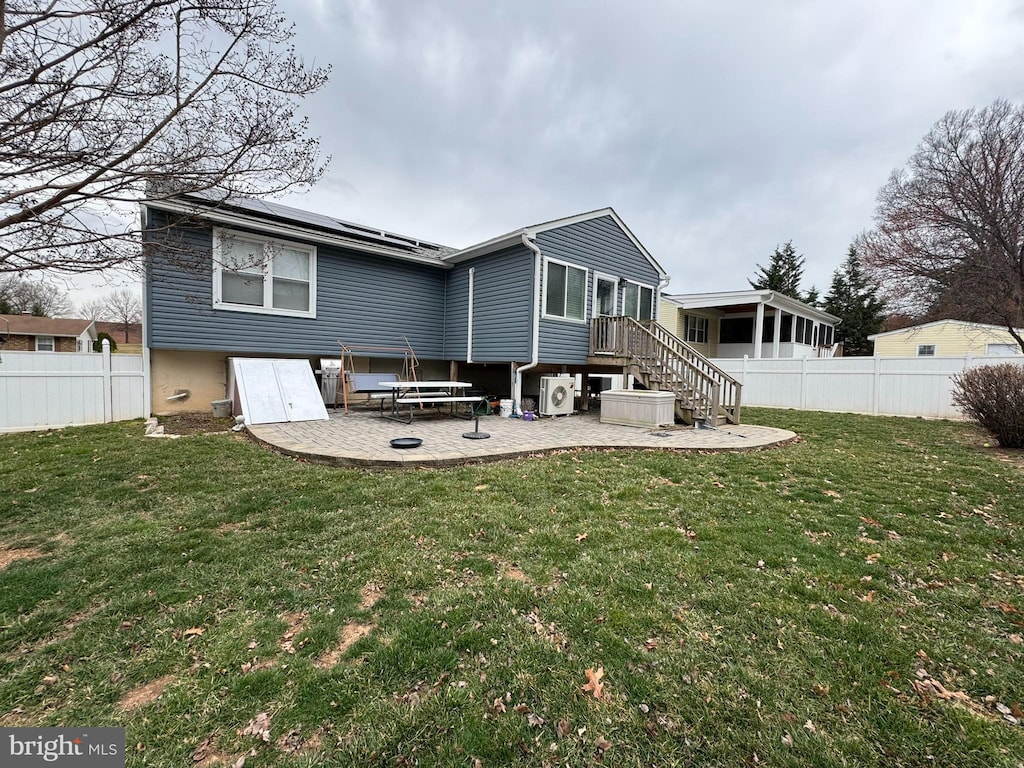 back of property with a yard, a fenced backyard, a patio, and roof mounted solar panels