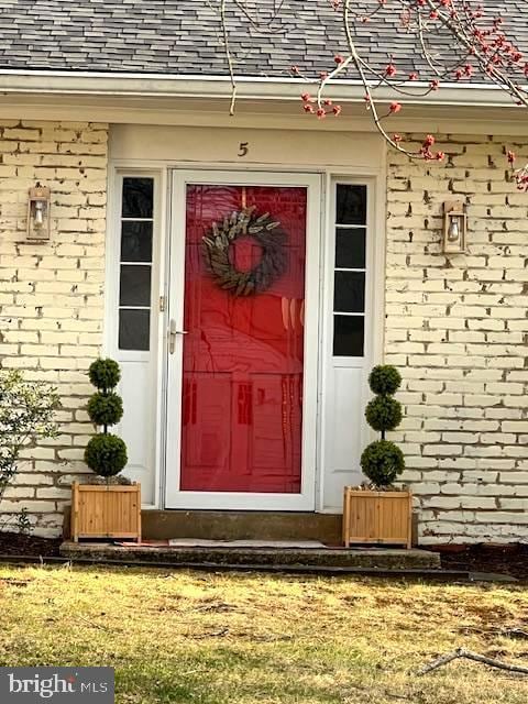 doorway to property featuring brick siding and roof with shingles