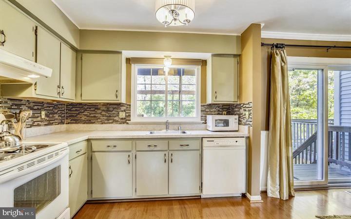 kitchen with a sink, under cabinet range hood, backsplash, white appliances, and light countertops