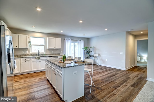 kitchen featuring stone counters, a kitchen island, stainless steel fridge with ice dispenser, white cabinets, and a kitchen breakfast bar
