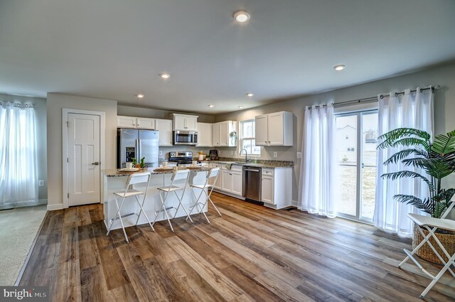 kitchen with a center island, appliances with stainless steel finishes, wood finished floors, white cabinetry, and a sink