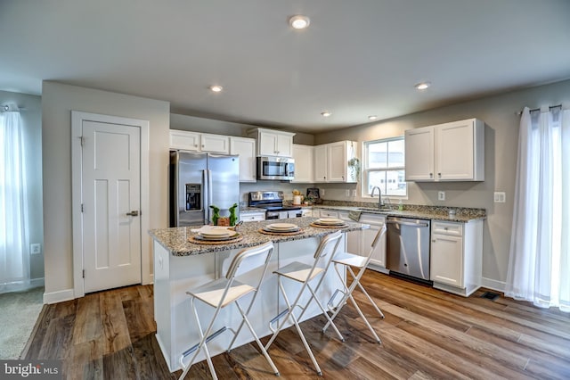 kitchen with dark wood-style floors, a center island, white cabinetry, appliances with stainless steel finishes, and light stone countertops