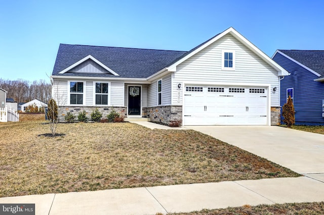 view of front facade featuring stone siding, a front yard, roof with shingles, and driveway