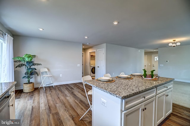kitchen with white cabinetry, washer / clothes dryer, dark wood-style flooring, dishwasher, and a kitchen breakfast bar