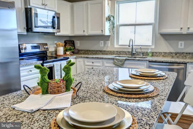 kitchen with a kitchen bar, light stone counters, appliances with stainless steel finishes, white cabinets, and a sink