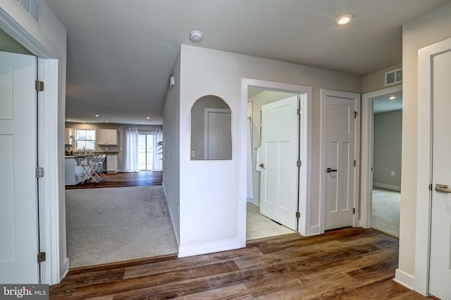 hall with carpet flooring, wood finished floors, visible vents, and baseboards