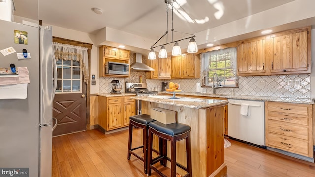 kitchen featuring appliances with stainless steel finishes, a kitchen island, light wood-style floors, and wall chimney range hood