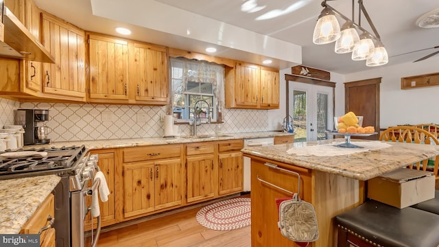 kitchen with a healthy amount of sunlight, gas stove, white dishwasher, a sink, and under cabinet range hood