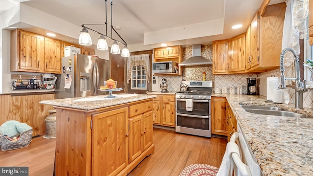 kitchen featuring a center island, light wood-style flooring, appliances with stainless steel finishes, wall chimney exhaust hood, and a sink